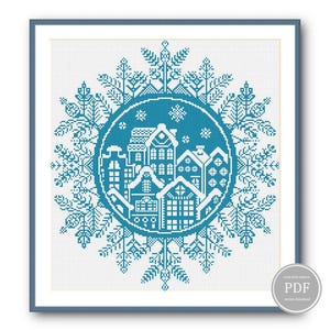 May include: A cross-stitch pattern featuring a blue snowflake design with a circle of houses inside. The houses are white with blue roofs and windows. The pattern is perfect for a winter-themed project.