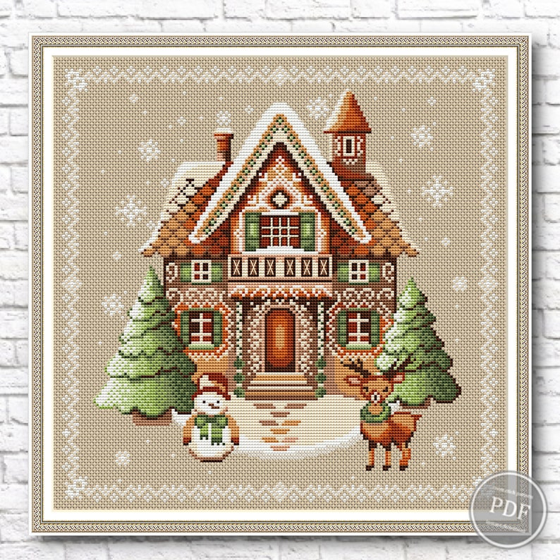 Gingerbread house cross stitch design with brown roof, green shutters, white trim, accompanied by snowman and two green trees on light brown background with white snowflakes.
