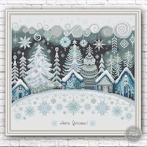 May include: A cross-stitch design featuring a winter landscape with snow-covered trees, houses, and snowflakes in shades of blue, white, and gray. The text "Merry Christmas!" is at the bottom. The design is framed.