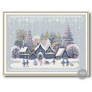 Può includere: Uno schema di punto croce che rappresenta una scena di un villaggio invernale con case blu, alberi coperti di neve e persone che camminano nella neve. Lo schema è incorniciato da una cornice blu chiaro e dorata.