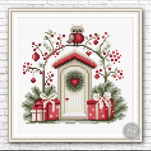 May include: Cross-stitch pattern featuring a festive scene. A red-roofed structure with a heart-shaped wreath is flanked by gift boxes and evergreen trees. An owl perches atop an arch adorned with red berries, creating a charming holiday design.