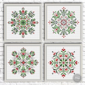 May include: Four square cross stitch patterns featuring symmetrical snowflake-like floral designs. Each pattern uses a grid of red, green, and black stitches on a white background, arranged in a two-by-two grid layout with light gray borders.