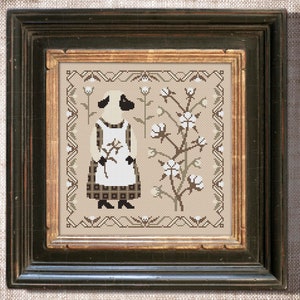 May include: A cross-stitch pattern featuring a black and white sheep wearing a plaid dress and apron, standing in a field of cotton plants. The pattern is framed in a dark wood frame.