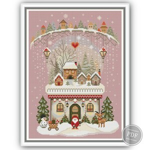 Pink background version of winter embroidery sampler with Nordic-style cottage, Christmas trees, gnome in red hat, reindeer, and snowman. Includes full pattern with festive winter elements, perfect for Christmas decor or stitching gifts.
