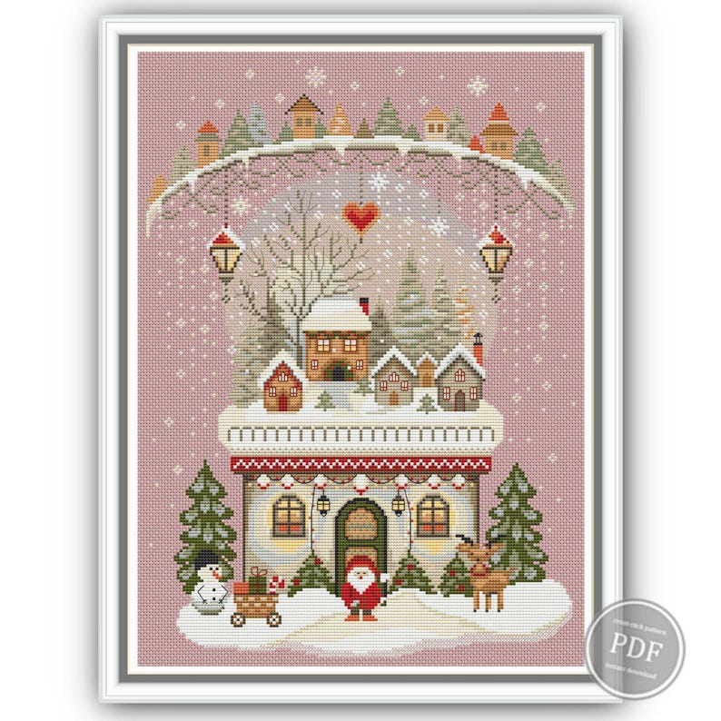Pink background version of winter embroidery sampler with Nordic-style cottage, Christmas trees, gnome in red hat, reindeer, and snowman. Includes full pattern with festive winter elements, perfect for Christmas decor or stitching gifts.