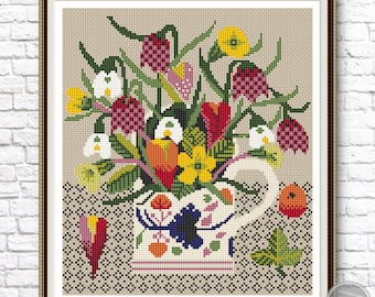 Puede incluir: Un patrón de punto de cruz que presenta un colorido ramo de flores en una jarra blanca con un diseño floral azul y verde. Las flores incluyen tulipanes rojos, narcisos amarillos, campanillas blancas y campanillas rosadas y rojas. La jarra está sentada sobre un fondo beige con un corazón marrón y una hoja verde.