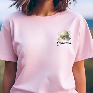 May include: Pink t-shirt with a green floral hat and the word "Grandma" printed on the front.