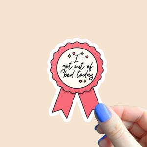 Könnte beinhalten: Ein rosa-weißer Aufkleber in Form eines Bandes mit dem Text "I got out of bed today". Der Aufkleber hat einen gewellten Rand und dekorative Herzen und Sterne.