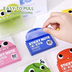 Könnte beinhalten: Ein Set aus bunten, rechteckigen Haftnotizspendern mit Cartoon-Monstergesichtern. Jede Box enthält 80 Blatt und zeigt den Text STICKY NOTE, 80 Sheets sowie den Markennamen Languo. Die Spender sind in Pink, Blau, Grün und Orange gehalten.