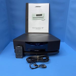 May include: A black Bose Wave SoundTouch music system with a digital display showing 5:43 and track 5. Included are a black remote control, a power cord, a USB cable, and an owner's manual with the text Bose Wave SoundTouch music system.