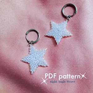 Puede incluir: Dos pendientes blancos en forma de estrella, hechos con cuentas y aros plateados. Los pendientes están hechos con pequeñas cuentas blancas y se muestran sobre una superficie de satén rosa. El texto "PDF pattern" y "Right Angle Weave" es visible.