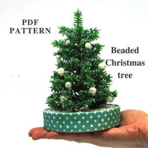 Könnte beinhalten: Ein Weihnachtsbaum aus Perlen mit weißen Perlen und einem türkisfarbenen Sockel mit weißen Punkten. Der Baum liegt auf einer Hand und der Text "PDF PATTERN" und "Beaded Christmas tree" ist sichtbar.