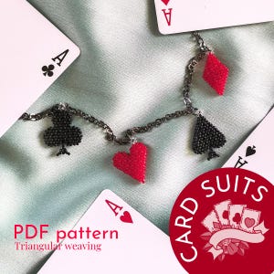 Puede incluir: Un collar de cuentas con colgantes con forma de palos de cartas: un trébol negro, un corazón rojo, un diamante rojo y una pica negra. El collar se muestra con naipes sobre un fondo de satén.