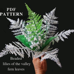 Peut inclure: Un arrangement floral perlé avec des feuilles de fougère argentées, des muguets blancs et des accents verts. Le texte "PDF PATTERN" et "Beaded lilies of the valley fern leaves" est inclus.