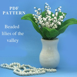 May include: PDF pattern for beaded lilies of the valley. The pattern shows a bouquet of white lilies with green leaves in a white vase. A string of white pearls is in the foreground.