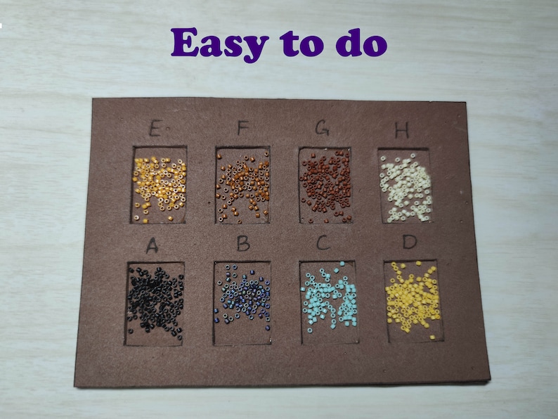 May include: A brown board with eight compartments, each containing a different color of small beads. The compartments are labeled with letters A through H. The text "Easy to do" is written in purple at the top of the board.