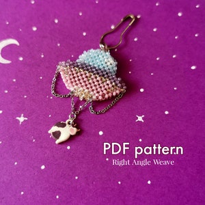 May include: A beaded pin with a layered design in shades of pink, purple, and blue, attached to a safety pin. A small cow charm hangs from the pin via a chain. The text "PDF pattern Right Angle Weave" is visible.