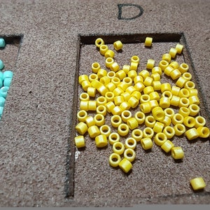 May include: A close-up of a yellow bead assortment in a square frame. The beads are small and round, and there are many of them.