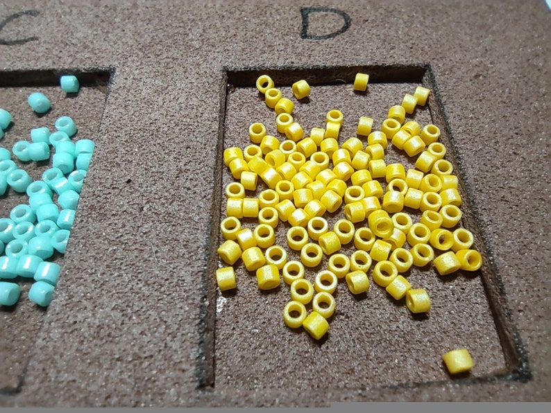 May include: A close-up of a yellow bead assortment in a square frame. The beads are small and round, and there are many of them.