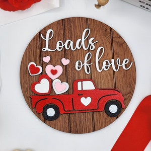 以下が含まれることがあります： 「Loads of love」と書かれた、赤いトラックがハートを積んでいる丸い木製の看板です。
