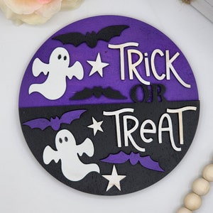 Może przedstawiać: Okrągły drewniany znak z fioletowym i czarnym tłem. Znak głosi "Trick or Treat" białymi literami i zawiera obrazy duchów i nietoperzy.