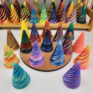 May include: A collection of colorful, cone-shaped decorative objects. Each cone features a spiral design and a variety of colors, including yellow, blue, pink, and orange. Some are displayed on a wooden stand.