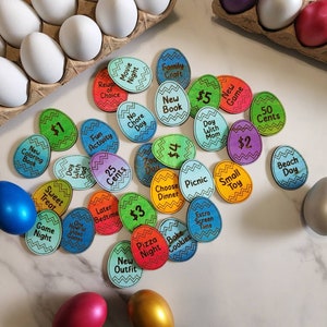 May include: A set of 20 colorful wooden eggs with different activities and rewards written on them. The eggs are decorated with zig-zag patterns and have a variety of colors, including blue, green, red, yellow, and orange. The text on the eggs includes phrases like "Movie Night", "New Book", "Fun Activity", "Sweet Treat", "Game Night", "One Hour of Video Games", "Later Bedtime", "$1", "$2", "$3", "$4", "$5", "25 Cents", "50 Cents", "Choose Dinner", "Picnic", "Extra Screen Time", "Bake Cookies", "Pizza Night", "New Outfit", "Day With Dad", "Day With Mom", "No Chore Day", "Beach Day", "Small Toy", "Family Craft", and "New Game".