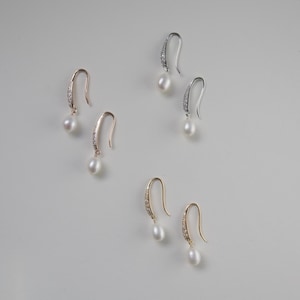 Könnte beinhalten: Drei Paar Perlen-Ohrringe mit einem gebogenen, mit Kristallen besetzten Stab. Die Ohrringe sind in Gold, Silber und Roségold erhältlich.