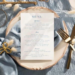 May include: A white menu card with blue text on a white plate with gold cutlery. The menu includes appetizers, main courses, and desserts. The text on the menu card reads: "MENU", "Appetizers", "Caprese Salad", "Fresh Mozzarella, ripe tomatoes, basil and a drizzle of balsamic reduction", "Shrimp Cocktail", "Grilled Filet Mignon", "Served with garlic mashed potatoes, roasted asparagus, and a red wine demi-glace", "Pan-Seared Salmon", "Accompanied by wild rice pilaf, sauteed spinach, and a lemon butter sauce", "Vegetarian Risotto", "Creamy risotto with wild mushrooms, parmesan, and a hint of truffle oil", "Dessert", "Vanilla Bean Creme Brulee", "Topped with fresh berries and caramelized sugar", "Chocolate Lava Cake", "Served with vanilla ice cream and a raspberry coulis"