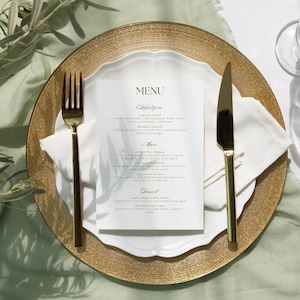 May include: A gold charger plate with a white plate on top. The white plate has a menu printed on it with the words "MENU", "Appetizers", "Main", and "Dessert". There are two gold utensils on the white plate, a fork and a knife. The charger plate is on a light green tablecloth.