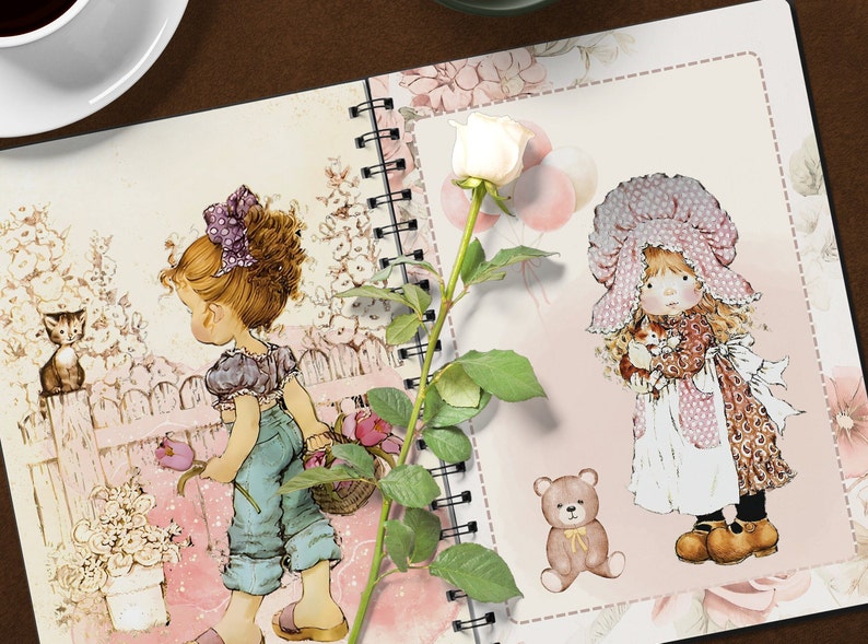 K&ouml;nnte beinhalten: Ein rosa-wei&szlig;es Notizbuch mit floralem Design und zwei Illustrationen von M&auml;dchen. Ein M&auml;dchen h&auml;lt einen Blumenkorb und das andere ein kleines K&auml;tzchen. Eine wei&szlig;e Rose mit gr&uuml;nen Bl&auml;ttern befindet sich auf der linken Seite des Notizbuchs.