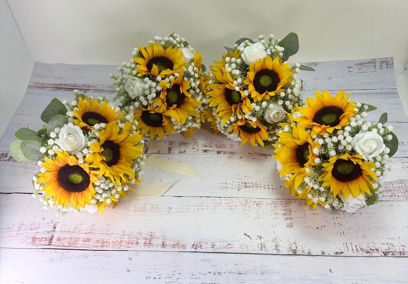 Pode incluir: Tr&ecirc;s ramos de flores com girass&oacute;is amarelo-brilhante, pequenas rosas brancas e delicadas flores de gips&oacute;fila brancas. Cada arranjo inclui folhas de eucalipto verdes e est&aacute; atado com uma fita de cor creme.