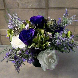 Könnte beinhalten: Ein Strauß aus lila und weißen Blumen, die in einer schwarzen Vase arrangiert sind. Der Strauß enthält Rosen, Hortensien und Lavendel.