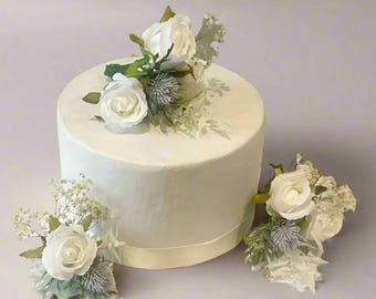 May include: Three white rose flower cake toppers with green leaves and white berries. The cake toppers are perfect for a wedding or special occasion.