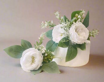 May include: Two white rose flower arrangements with green leaves and stems. The flowers are on a white cake.