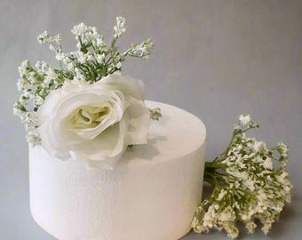 May include: A white cake dummy with a single white rose and baby's breath floral arrangement on top.