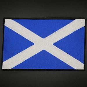 May include: A rectangular patch displaying the Scottish flag, the Saltire. The flag features a blue field with a white diagonal cross. The patch is edged with a black border.
