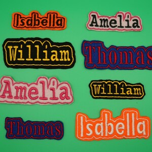 May include: Eight embroidered iron-on patches with different names, including Isabella, Amelia, William, and Thomas. The patches are in various colours, including orange, pink, black, blue, and yellow.