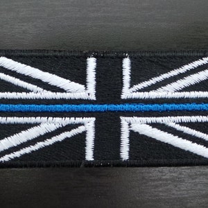 May include: Embroidered patch depicting the Union Jack flag with a blue line. The patch has a black background with white and blue stitching. The design is rectangular.