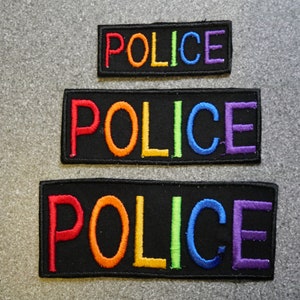 May include: Three black patches with the word "POLICE" embroidered in rainbow colours. The patches are different sizes, with the largest at the bottom and the smallest at the top.