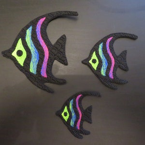 May include: Three black felt fish with colourful stripes and a green eye. The fish are different sizes and are arranged in a triangular pattern.