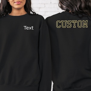 以下が含まれることがあります： 黒のトレーナーで、背面に「CUSTOM」という文字が金色の輪郭で描かれており、前面には「Text」という文字が書かれています。