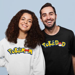 Puede incluir: Una mujer con una sudadera blanca con la frase "Pokémon Mom" en letras amarillas y azules. Un hombre con una camiseta negra con "PokéDad" en amarillo y azul. Ambas prendas presentan un diseño de Pokéball rojo y blanco.