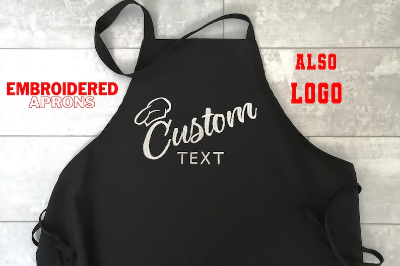 Puede incluir: Delantal negro con texto bordado blanco "Custom TEXT" y un dise&ntilde;o de gorro de chef. El delantal tiene una correa para el cuello y lazos. Las palabras "EMBROIDERED APRONS" y "ALSO LOGO" est&aacute;n en texto rojo.