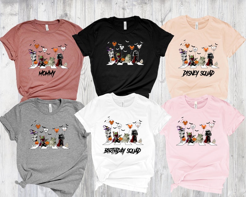 Puede incluir: Una colecci&oacute;n de seis camisetas de manga corta en varios colores, cada una con un gr&aacute;fico de personajes de Star Wars cruzando una calle, con globos tem&aacute;ticos de Halloween y Disney. Las camisetas tienen el texto "MOMMY", "DISNEY SQUAD" y "BIRTHDAY SQUAD".