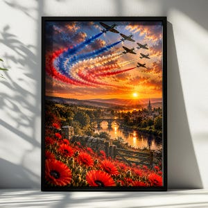 Op de afbeelding: Een ingelijste kunstdruk met een zonsonderganglandschap, een veld met rode klaprozen op de voorgrond, een rivier met een stenen brug en een formatie van zes vintage propellervliegtuigen die rode en blauwe rooksporen in de lucht achterlaten.