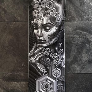 May include: A black and white skateboard deck with a geometric design featuring a stylized face with a hexagonal pattern. The face is surrounded by a complex pattern of geometric shapes.