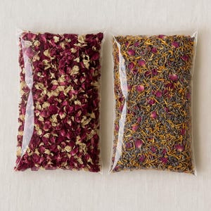 May include: Two clear plastic bags filled with dried flower petals. One bag contains a mix of burgundy and cream-colored petals. The other bag has a mix of purple, orange, and pink petals. The bags are sealed and ready for use.