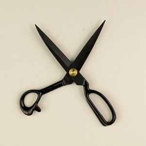 Könnte beinhalten: Schwarze Schere mit goldenen Akzenten. Die Klingen sind geschlossen und die Griffe sind gekreuzt.