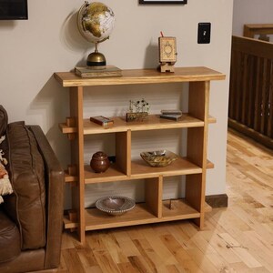 May include: A light wood bookshelf with four shelves and a top surface. The shelves are divided into sections with some open and some closed. The bookshelf is decorated with a globe, a small box, a bowl, and a small plant.